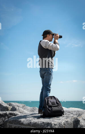 Homme avec un appareil photo sur des roches par la côte Banque D'Images