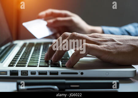 Homme tenant une carte de crédit en main et entrer le code de sécurité à l'aide de smart phone sur clavier d'ordinateur portable, le magasinage en ligne concept. Banque D'Images