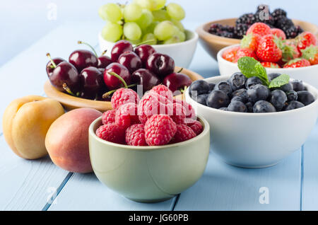 Une sélection de différents fruits d'été, dans une variété de coupes sur un bois peint bleu ferme planches dont la table de cuisine, contre un fond bleu clair. Banque D'Images