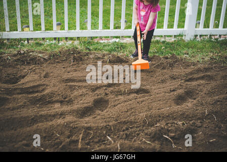 Un bambin permet d'hoe un jardin dans une cour. Banque D'Images