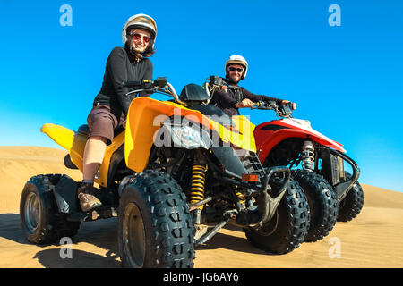 Quad conduisant des personnes - happy smiling couple bikers en désert de sable. Banque D'Images