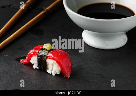 Nigiri thon rouge à l'algue nori et pâte de wasabi sur noir ardoise avec des baguettes et un bol de sauce de soja. Le poisson cru dans les sushis japonais traditionnel Banque D'Images