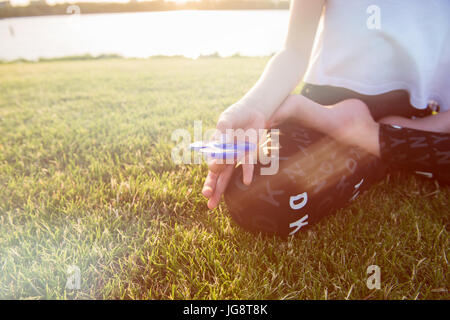 Un adolescent girl in lotus pose avec les bobines. Fille avec un tri Fidget part Spinner sur sa main à l'extérieur. L'herbe verte à l'arrière-plan. Banque D'Images