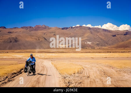 Cycliste femme aux prises et en poussant son vélo sur la route de sable en carton ondulé de l'Altiplano en Bolivie Banque D'Images