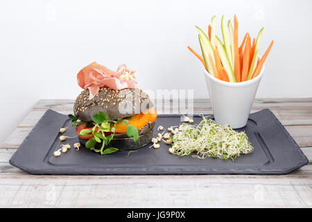 Burger sain avec hamon, tomates, pousses et noir, petits pains à grains entiers de bâtonnets de légumes sur la plaque en ardoise noire sur fond de bois. Nettoyer, alimentaires, les régimes alimentaires detox concept. Banque D'Images