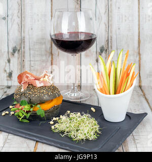 Burger sain avec hamon, tomates, pousses et noir, petits pains à grains entiers de bâtonnets de légumes et de vin rouge à l'ardoise noire sur fond de bois. Nettoyer, alimentaires, les régimes alimentaires detox concept. Banque D'Images