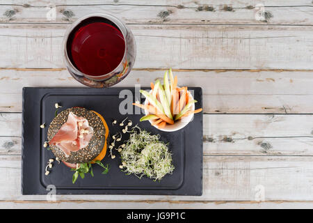 Burger sain avec hamon, tomates, pousses et noir, petits pains à grains entiers de bâtonnets de légumes et de vin rouge à l'ardoise noire sur fond de bois. Nettoyer, alimentaires, les régimes alimentaires detox concept. Banque D'Images