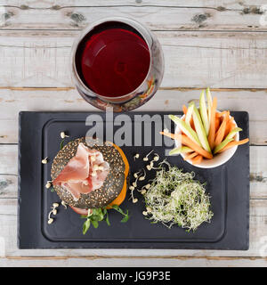 Burger sain avec hamon, tomates, pousses et noir, petits pains à grains entiers de bâtonnets de légumes et de vin rouge à l'ardoise noire sur fond de bois. Nettoyer, alimentaires, les régimes alimentaires detox concept. Banque D'Images