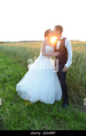 Couple marié est frais s'embrassent alors que le coucher du soleil à l'extérieur dans un champ Banque D'Images
