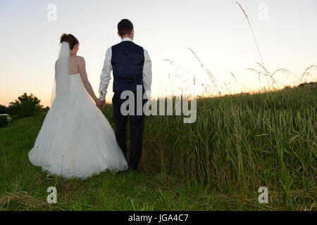 Jeune couple à l'arrière debout dans un champ et regardant le coucher du soleil Banque D'Images