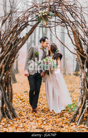 Couple de mariage merveilleux regarder avec amour les uns les autres sous le noisetier arch dans forêt d'automne Banque D'Images