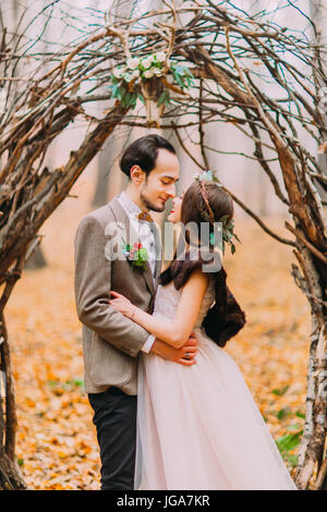 Charmant couple de mariage élégant serrant doucement sous hazel romantique arch dans forêt d'automne Banque D'Images