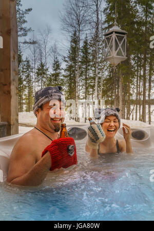 Couple dans un bain à remous de déguster une boisson, Laponie, Finlande Banque D'Images