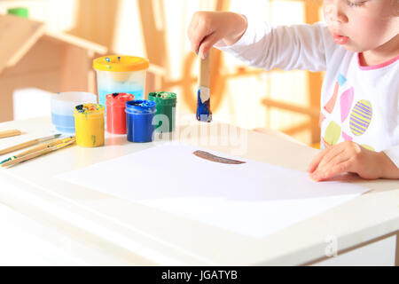 Enfant avec un pinceau dans la peinture s'inspire. Petite fille à l'aide de peinture pour l'art. Banque D'Images