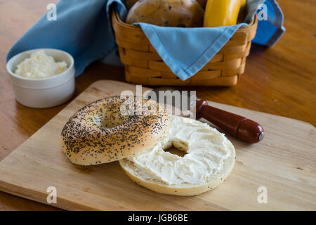 Poppy seed bagel avec fromage à la crème avec un panier d'un assortiment de bagels en arrière-plan. Banque D'Images