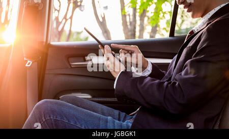 Young handsome businessman working en arrière de voiture et à l'aide d'une tablette ou un téléphone intelligent. Banque D'Images