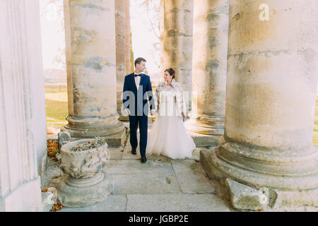 Les nouveaux mariés sont main dans la main tout en marchant entre les colonnes de l'ancienne église. Banque D'Images
