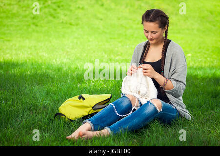 Jeune femme à la mode tricote un chandail blanc sur un tricot vert lumineux sur l'herbe un jour d'été Banque D'Images