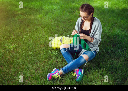 Jeune femme à la mode d'un chandail vert knits knitting sur l'herbe verte un jour d'été Banque D'Images