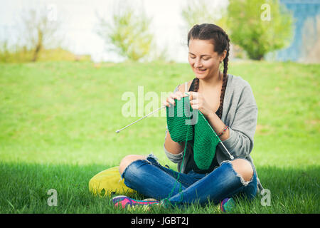 Jeune femme à la mode d'un chandail vert knits knitting sur l'herbe verte un jour d'été Banque D'Images