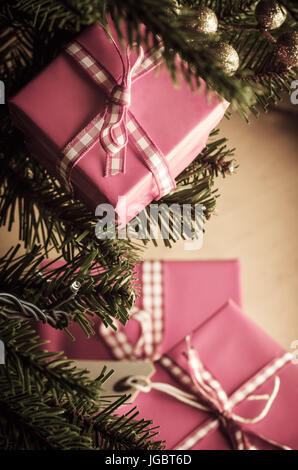 Cadeaux de Noël rose dans les succursales et autour de la base d'un arbre décoré, enveloppés dans du ruban vichy et attaché avec des arcs. Tourné à partir de ci-dessus et à la faire Banque D'Images