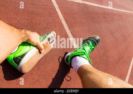 Un athlète épuisé sur une piste de course portant des chaussures de course verte cassée avec de grands trous dans la semelle. Banque D'Images