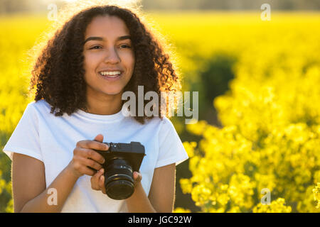 Beautiful happy mixed race African American girl adolescent femme jeune femme smiling outdoors dans sunshine de prendre des photographies avec un appareil photo Banque D'Images