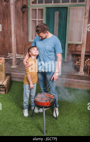 Smiling père et fils la cuisson hamburgers et saucisses hot-dog sur barbecue Banque D'Images