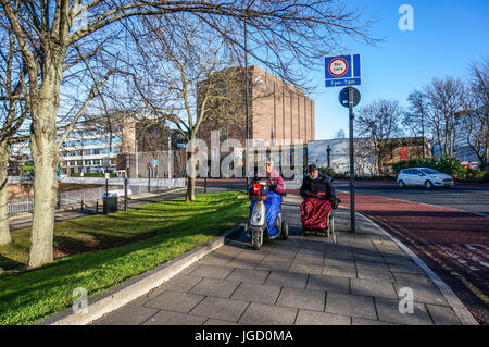 Un vieux / personnes âgées, handicapées couple riding leur mobilité scooters sur le trottoir, Liverpool City Centre. Tyne et Wear, Angleterre, Royaume-Uni. Banque D'Images