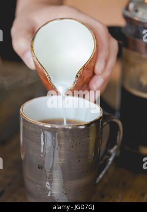 Young woman pouring lait en faïence brune brown tasse de café filtré. Close up, composition verticale, faible profondeur de champ Banque D'Images