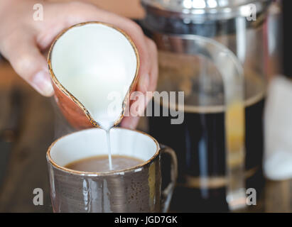 Young woman pouring lait en faïence brune brown tasse de café filtré. Close up, composition horizontale, faible profondeur de champ Banque D'Images