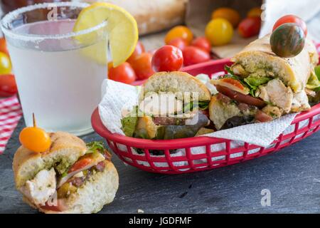 Revenons sur un pique-nique ! Sandwichs au poulet grillé gastronomique servi avec petits pains français, nappe rouge à carreaux rouges et prenez-out panier - Yum ! Banque D'Images