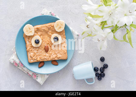 Petit-déjeuner / snack / école le déjeuner pour les enfants : le beurre d'arachides rôties avec banane, myrtille et amandes aussi drôle en forme de hibou sur plaque bleue. Vue d'en haut Banque D'Images