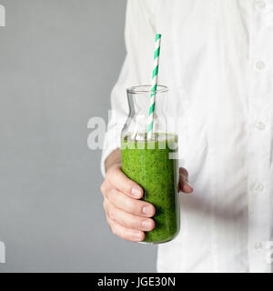 Jeune homme tenant une bouteille de green smoothie détox avec paille. Les carrés. Concept de vie sain, une alimentation saine Banque D'Images