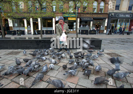 Seul un homme habillé excentrique pigeons d'alimentation sur une place assise sur un banc à Glasgow Banque D'Images