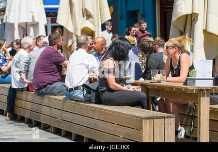 Les gens assis dehors sur des tables en bois et bancs pour un café et un bar sur une chaude journée d'été. Banque D'Images