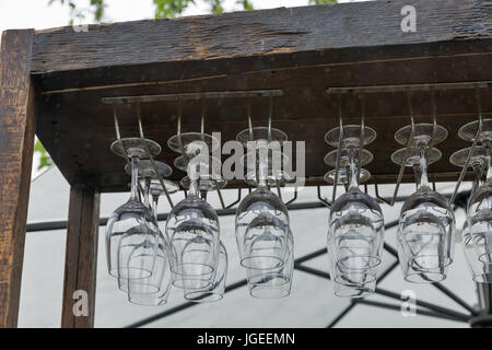 Une rangée de verres à vin, accroché sur un rack en bois de terrasse de restaurant extérieur sous la pluie. Banque D'Images