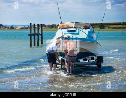 Deux hommes tirant une petite embarcation à moteur hors de la mer le long d'un halage. Banque D'Images