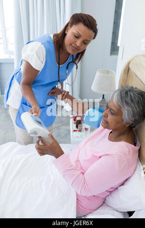 Femme médecin la mesure de la pression artérielle de senior woman in bedroom Banque D'Images