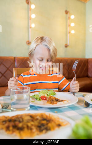 Smiling boy ayant la nourriture en sitting in restaurant Banque D'Images