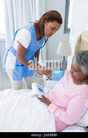 Femme médecin la mesure de la pression artérielle de senior woman in bedroom Banque D'Images