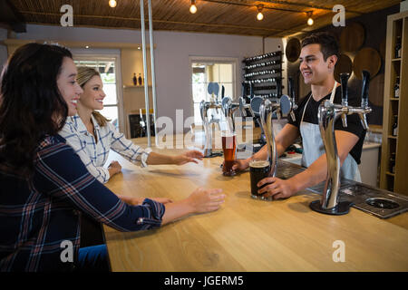 Barman qui sert des boissons à female friends at counter in restaurant Banque D'Images