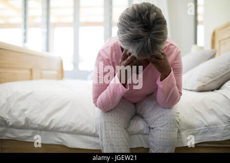 Tendue senior woman sitting on lit dans la chambre à la maison Banque D'Images