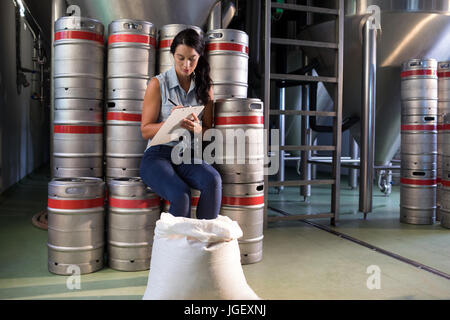 Travailleur féminin writing on clipboard while sitting in factory Banque D'Images