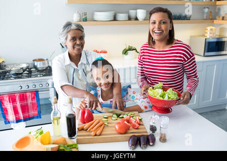 Portrait of smiling grandmother aider sa petite-fille à couper les légumes dans la cuisine à la maison Banque D'Images