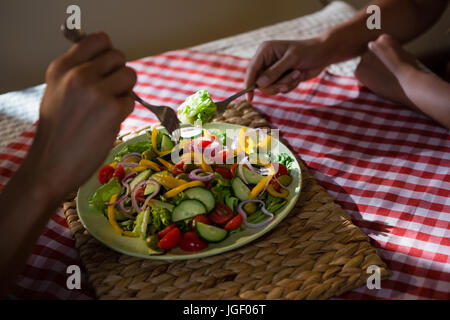 Mains coupées d'amis ayant salade à table dans un restaurant Banque D'Images