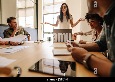 Shot of young businesswoman giving presentation de ses collègues assis autour de la table dans la salle de conférence. Multi ethnic business people during meeting Banque D'Images