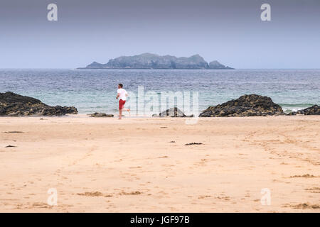 Un homme qui court le long de la plage à Harlyn Bay avec Gulland Island en arrière-plan. Nord de Cornwall. Banque D'Images