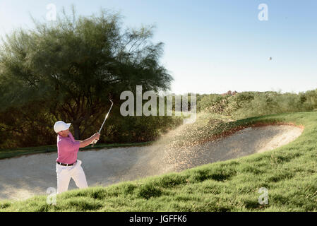 Golfeur hispaniques hitting ball en fosse de sable Banque D'Images