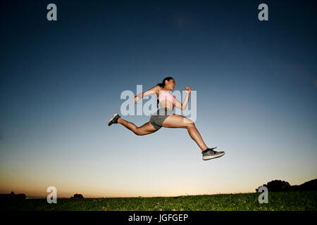 Mixed Race woman courir et sauter dans la zone au coucher du soleil Banque D'Images